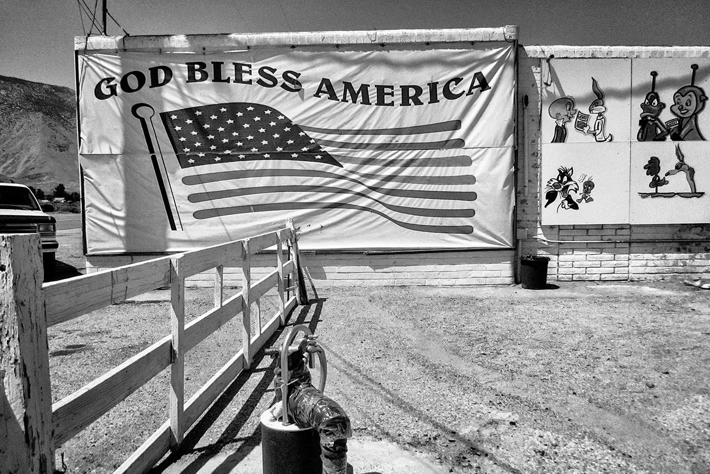Back and white photo of a God Bless America sign next to Loony Toons characters.