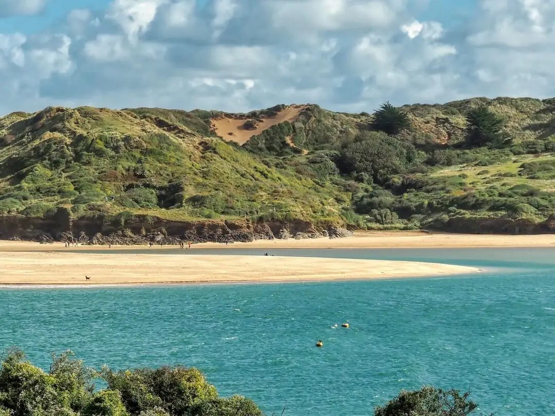 A spit of sand sits between the sea and green hills in the background
