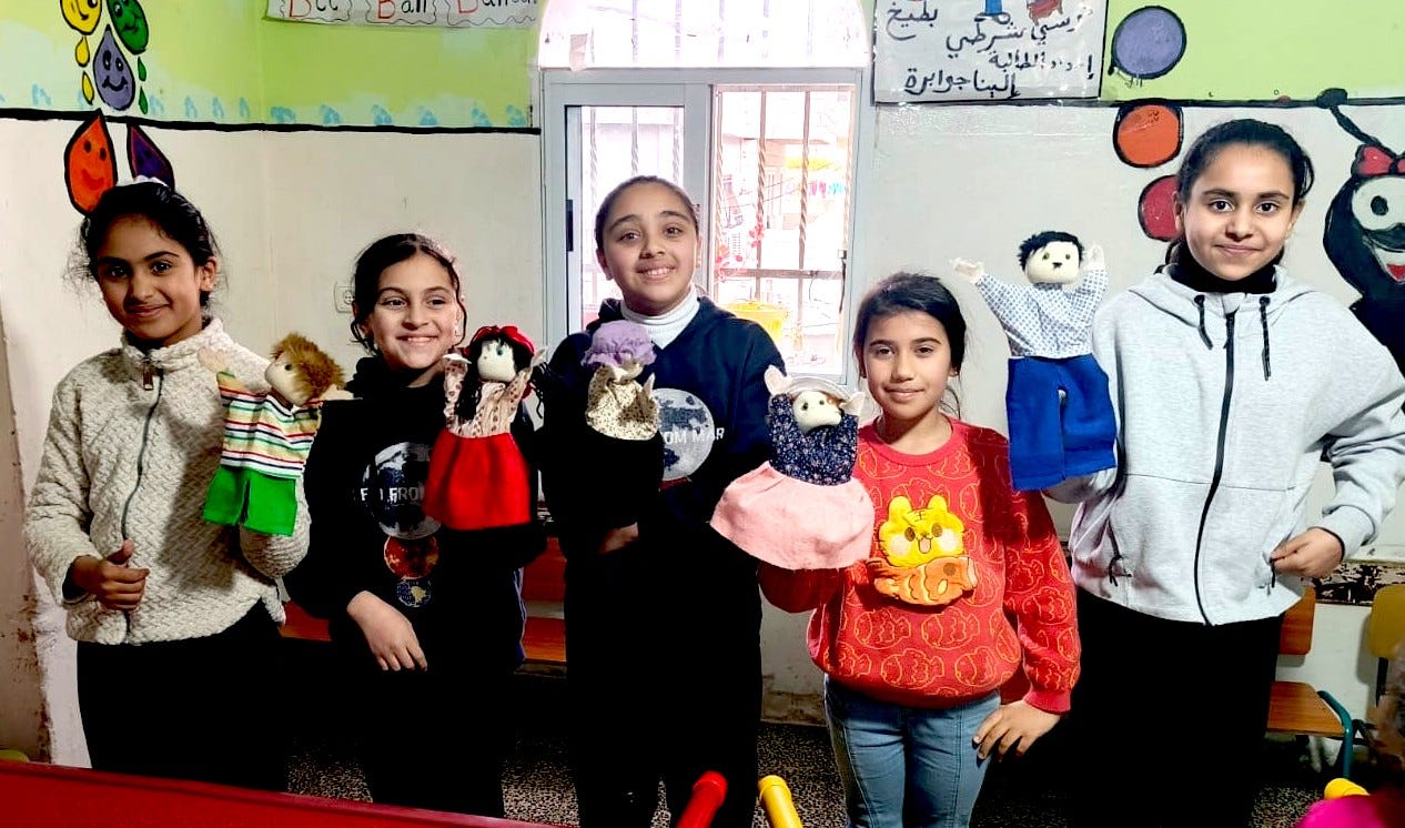 Four Palestinian girls, about 10 years old, stand smiling as they hold puppets for their theater project.