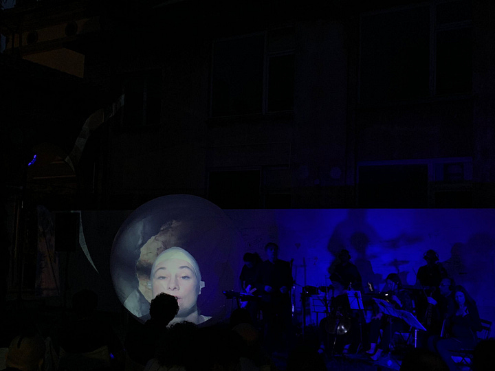 Nell'immagine si vede il gruppo musicale di A. Zannier suonare di sera davanti al pubblico, con una scenografia di luci e installazioni