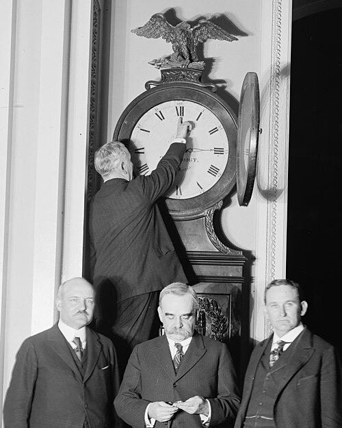 Black-and-white photo of a man adjusting an ornate eagle-topped clock while three suited men stand below. Black-and-white photo of a man adjusting an ornate eagle-topped clock while three suited men stand below.