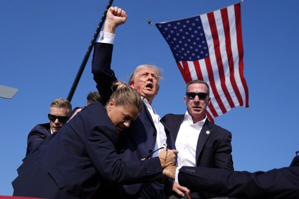 Trump raising his fist while surrounded by secret service agents, blooding dripping down his cheek and an American flag waving in the background.