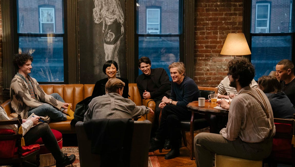 Diverse group of people gather on a leather sofa and chairs in a dimly lit, brick-walled studio for a lively discussion.