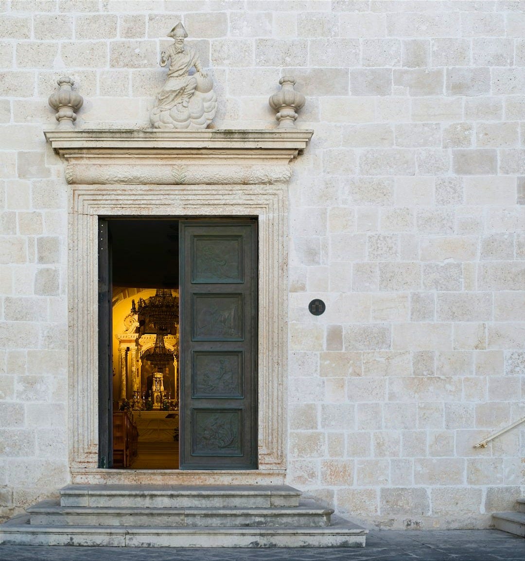 Ornate doorway of a stone building, one side open, the other closed.