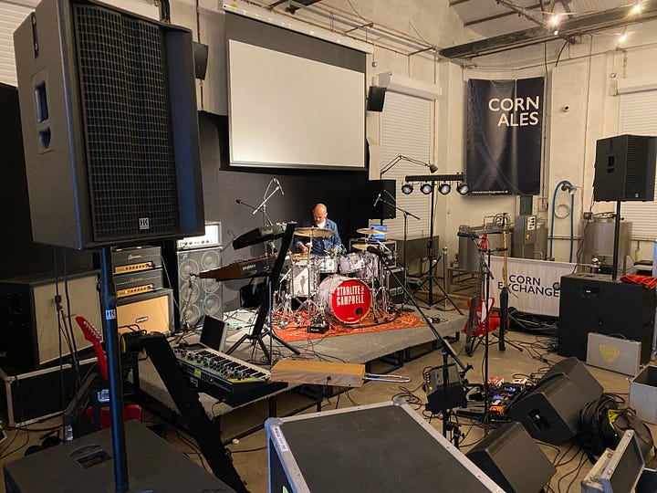 Inside a big warehouse style venue with stage and musical equipment. Stef from Pukka PA Hire setting up
