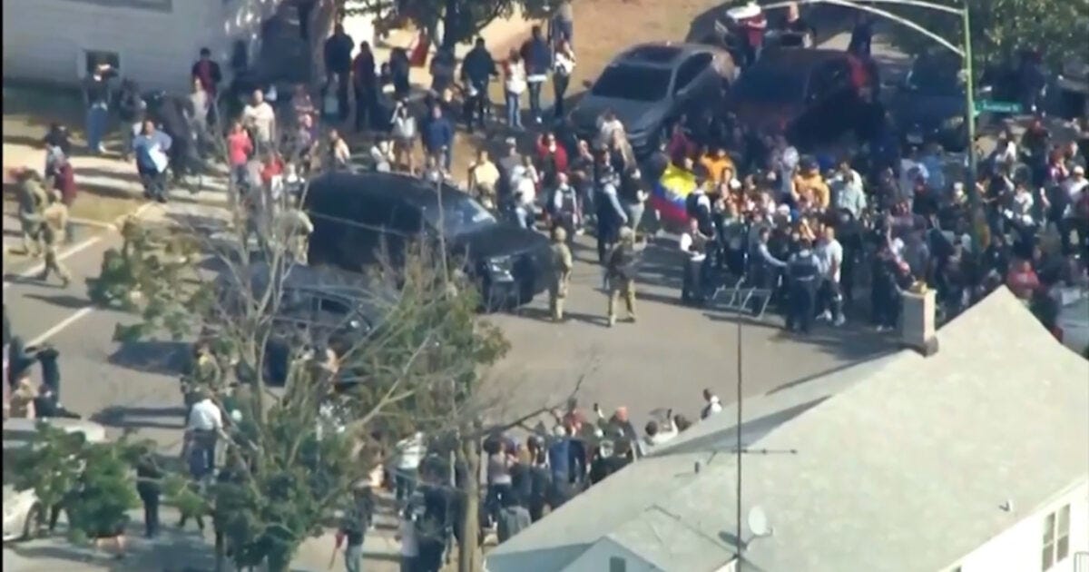 Crowd gathered on a street with law enforcement presence, surrounded by vehicles, during a significant public event or protest.