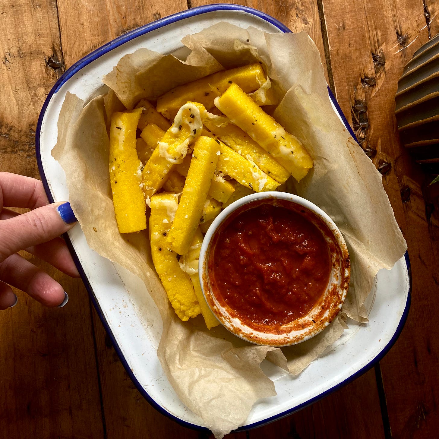 Overhead shot of a dish filled with polenta chips and a ramekin of tomato sauce