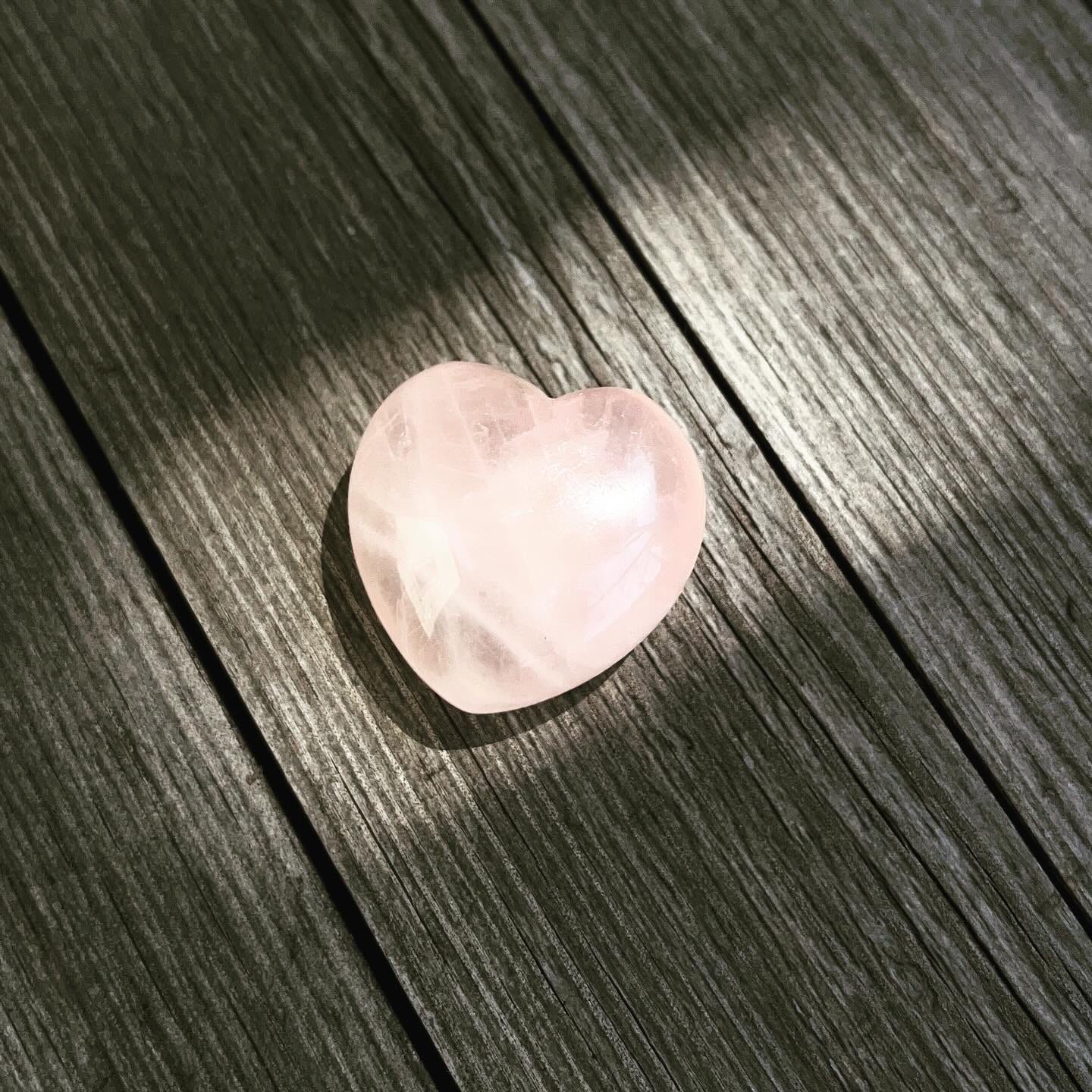 A photograph of the rose quartz heart in a beam of sun on the wooden table