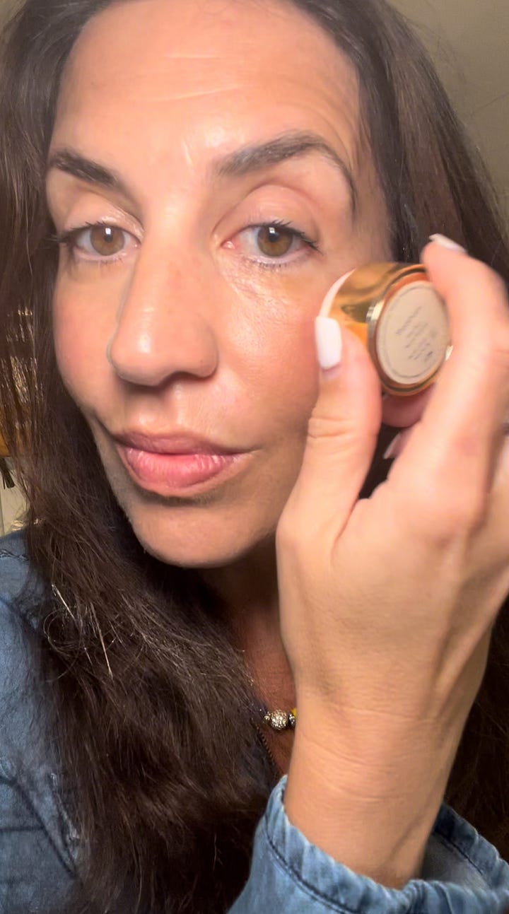 A close-up of the Sweed Cloud Mascara wand and tube held in front of a tote bag that says "The Beauty Ed."A woman applying a cream beauty product from a luxury gold-capped pot to her under-eye area.