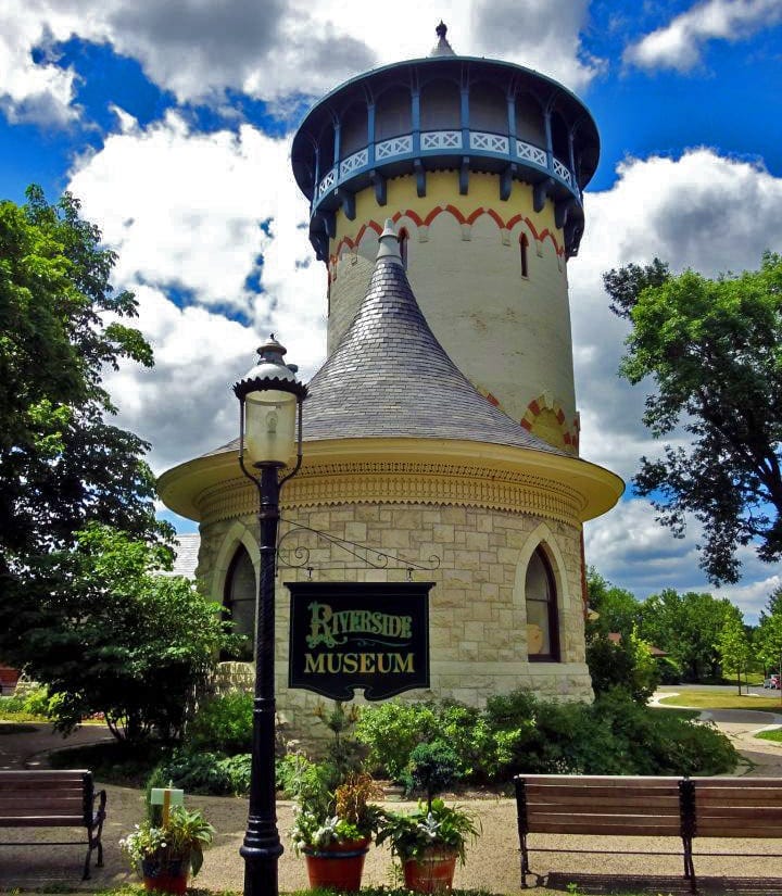 Gas streetlight in foreground with sign that reads Riverside Museum. Circular white brick building behind it. In the back, a cream-colored Gothic water tower. Gas streetlight in foreground with sign that reads Riverside Museum. Circular white brick building behind it. In the back, a cream-colored Gothic water tower.