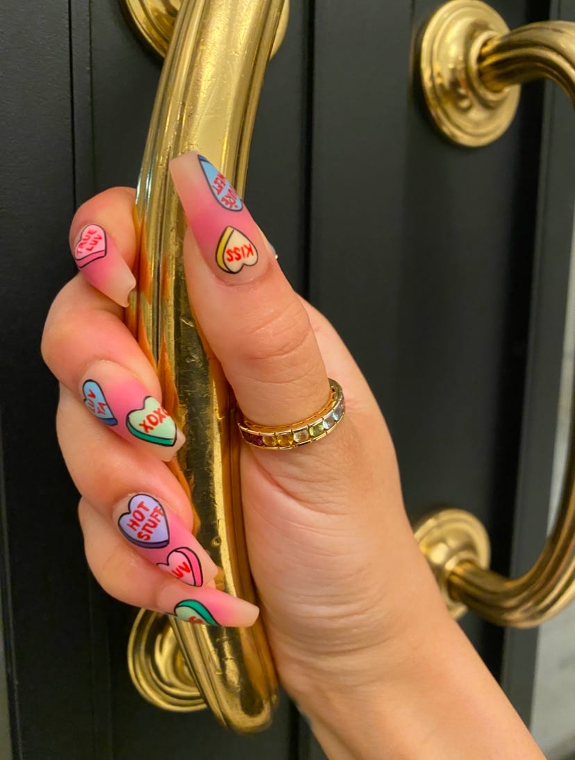Kiana's hand with conversation heart press on nails, holding a golden door handle