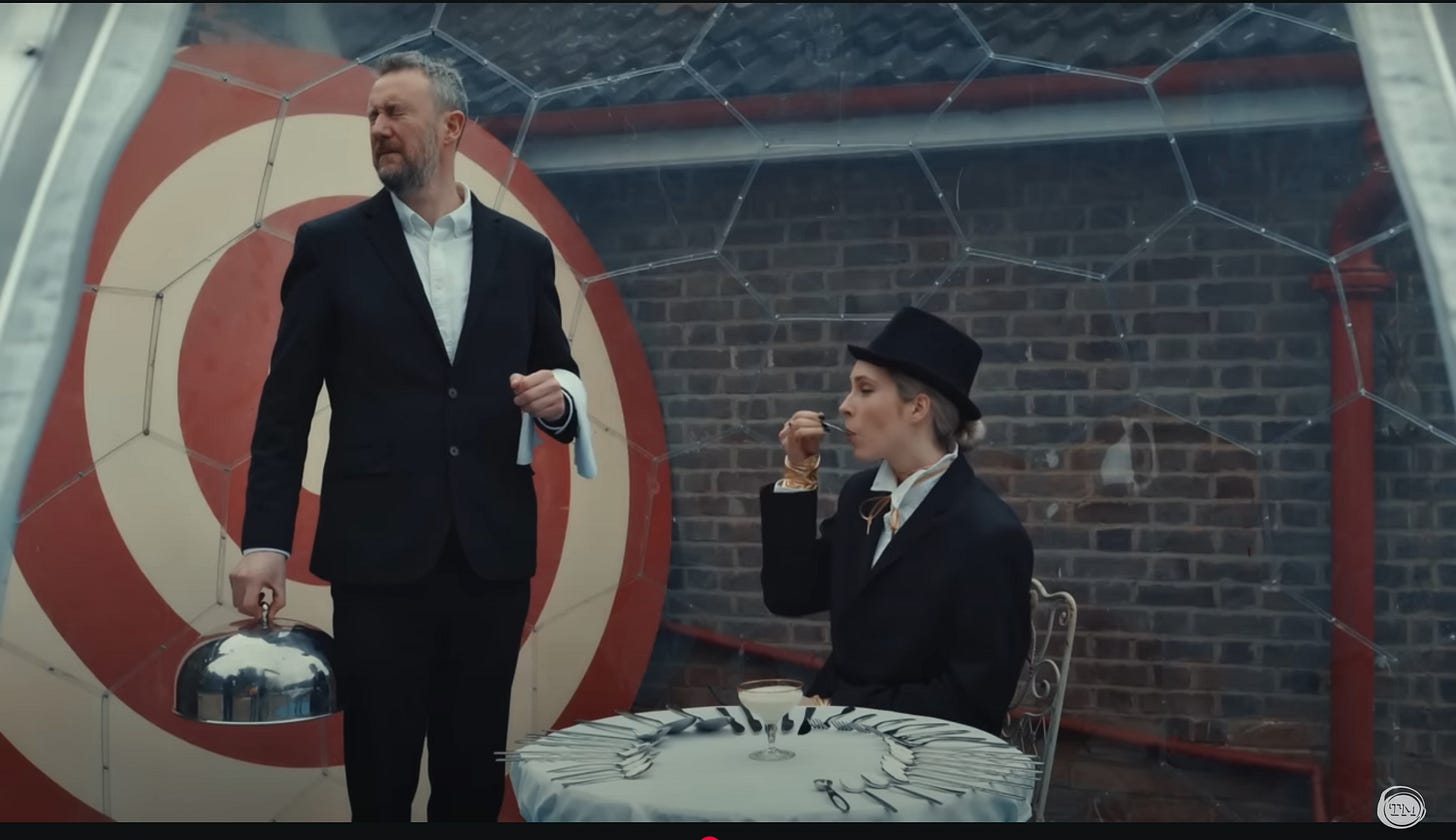 Little Alex Horne squints his eyes and looks away as Stevie Martin uses a tiny spoon to taste yogurt.