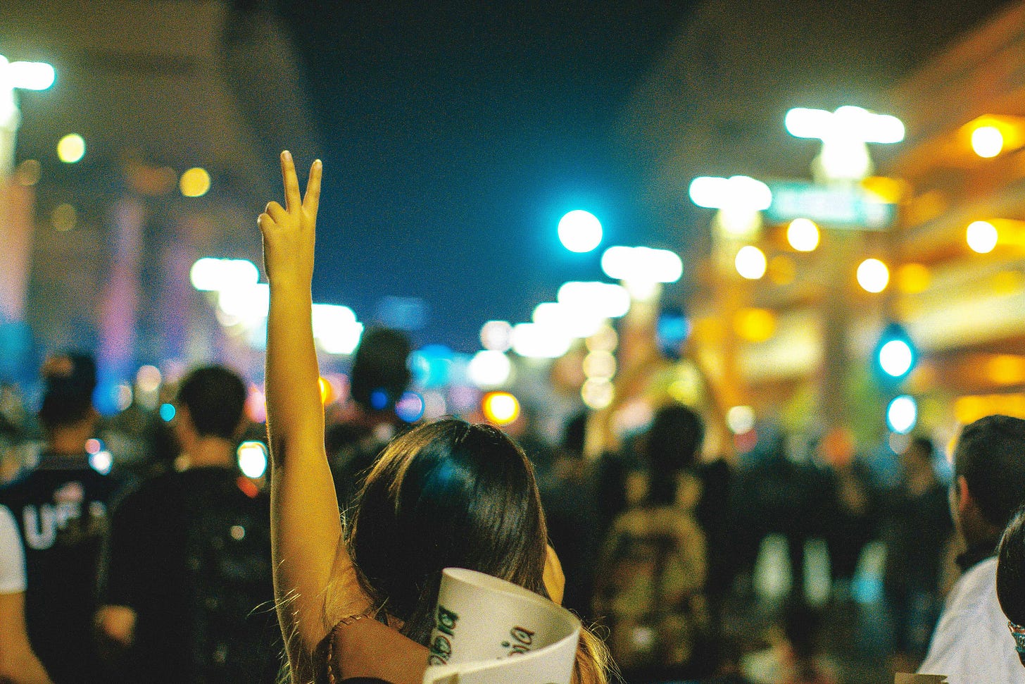 people marching in protest, a person flashing a peace sign people marching in protest, a person flashing a peace sign