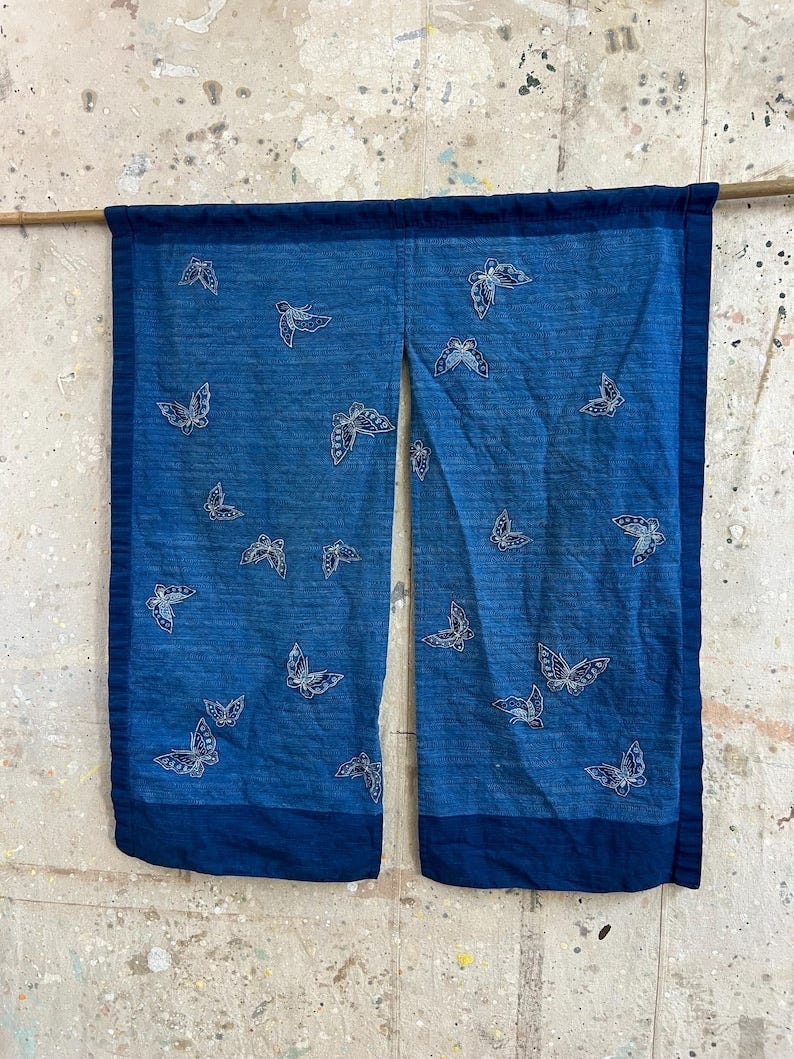 May include: Indigo blue fabric panel with white butterfly designs. The panel is divided into two sections, each featuring a dark blue border. The butterflies are scattered across the fabric, creating a decorative textile.