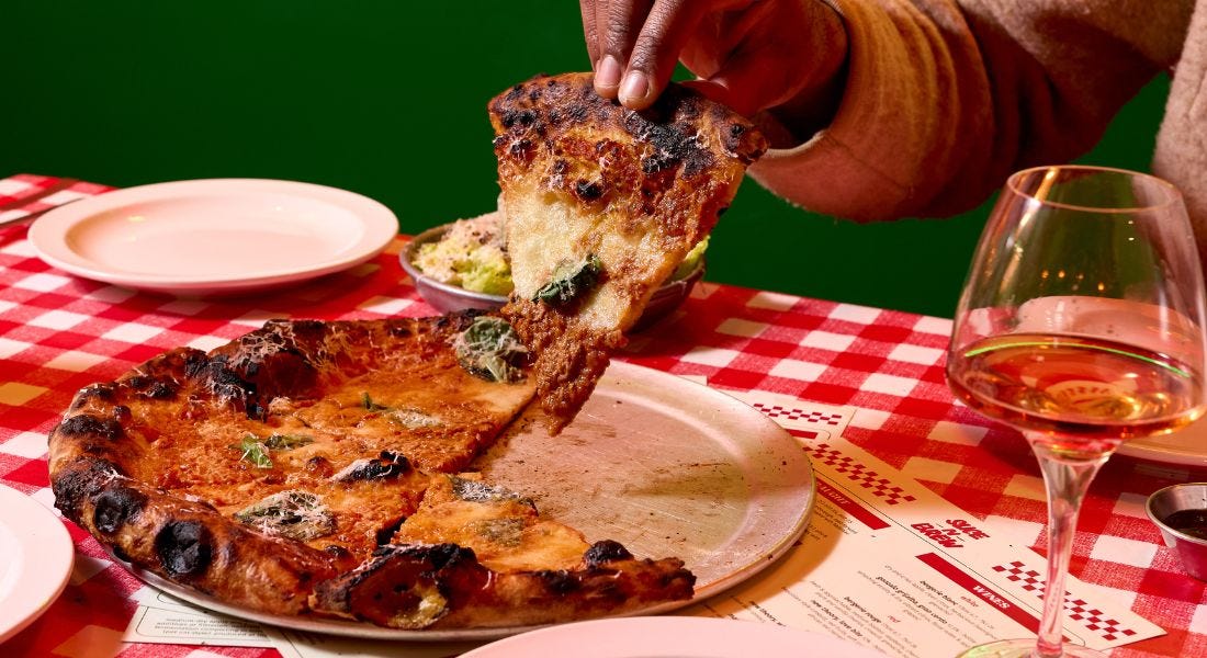 A plate of cheese pizza with a hand above it holding a slice, on top of a red and white checked tablecloth with white plates on it, and a green wall behind it A plate of cheese pizza with a hand above it holding a slice, on top of a red and white checked tablecloth with white plates on it, and a green wall behind it