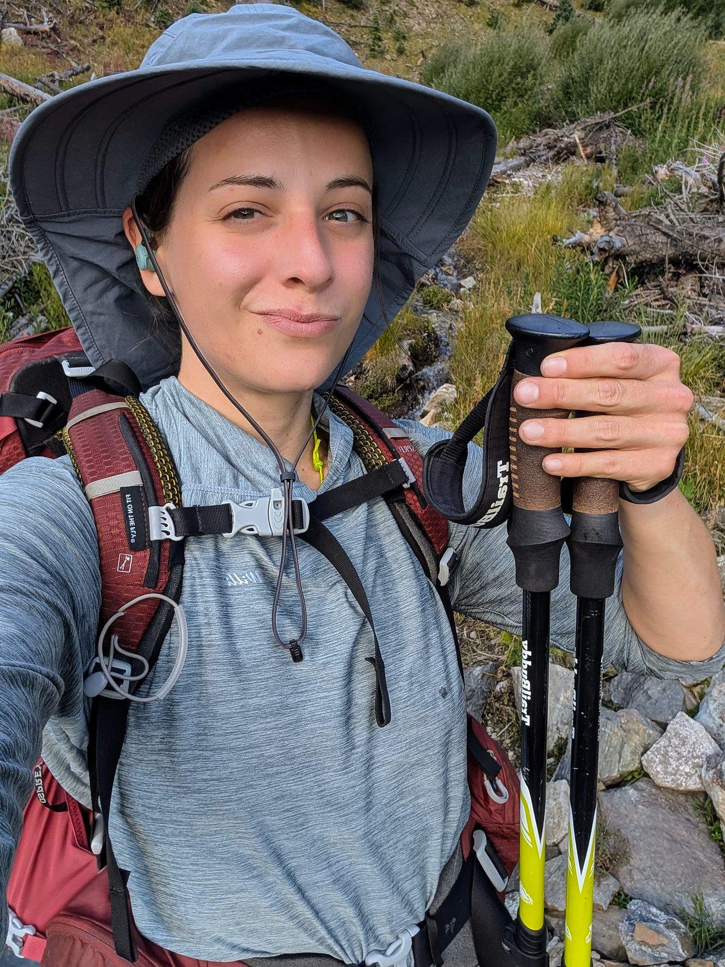 Selfie of hiker Freda Heights in a wide-brim sun hat holding trekking poles, wearing a maroon pack on a rocky trail. Selfie of hiker Freda Heights in a wide-brim sun hat holding trekking poles, wearing a maroon pack on a rocky trail.
