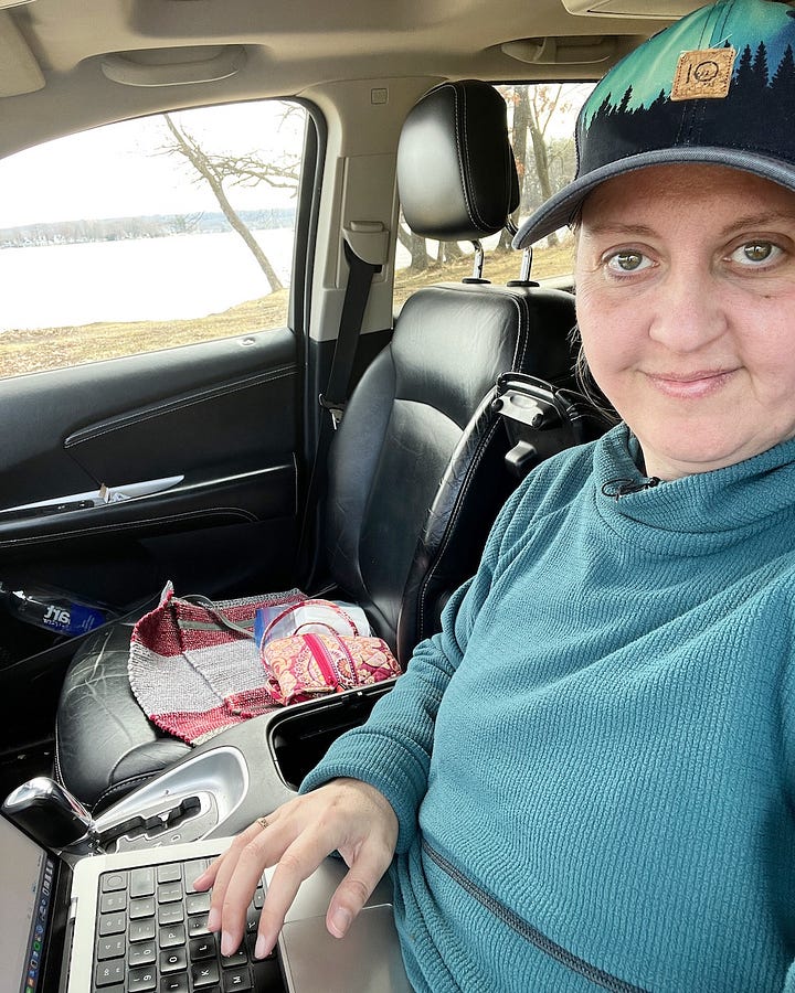 author sitting in car with laptop writing book with a view of the lake in the background