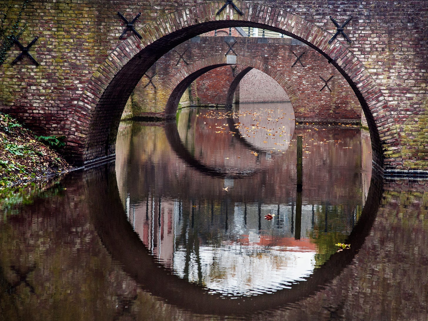 A series of old brick arch bridges reflected in still water, creating layered circular shapes.
