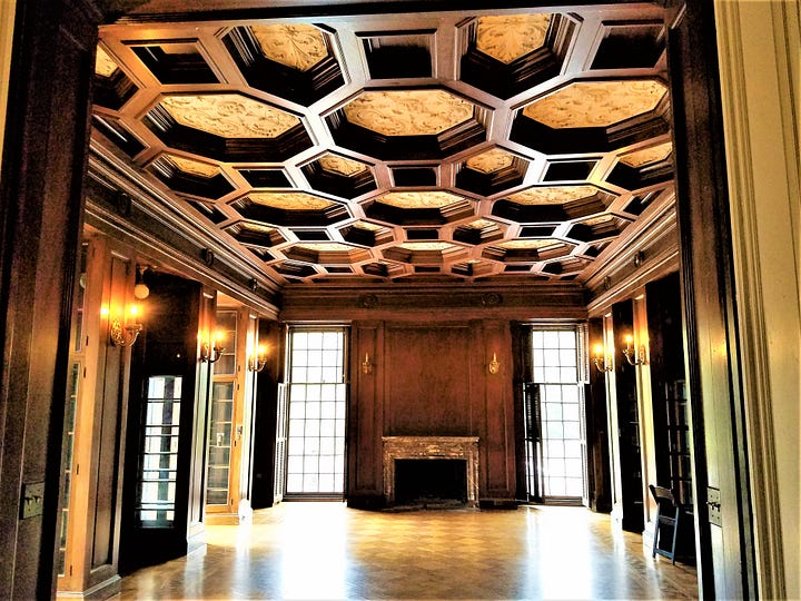 A room with an ornate wood ceiling, wooden walls and fireplace, with a closeup of the ceiling.