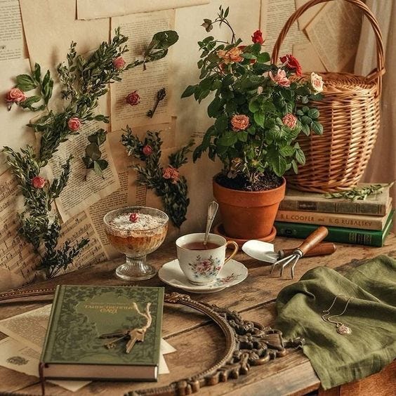 A picture of a bench with several objects on it including a cup of tea on a saucer, a trowel, a parfait in a glass dish, a book with a green cover, a pot plant, a basket, a green cloth with a pendant necklace on it, and several yellowing pages of text pinned to the wall behind with flowers A picture of a bench with several objects on it including a cup of tea on a saucer, a trowel, a parfait in a glass dish, a book with a green cover, a pot plant, a basket, a green cloth with a pendant necklace on it, and several yellowing pages of text pinned to the wall behind with flowers