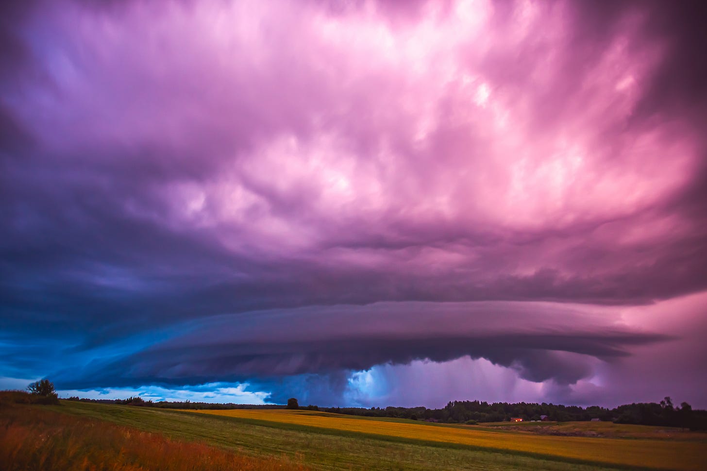 Massive super-cell stormy sky with pink and purple clouds over fields