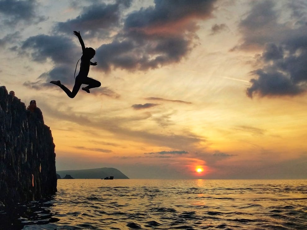silhouette of man jumping on sea during sunset