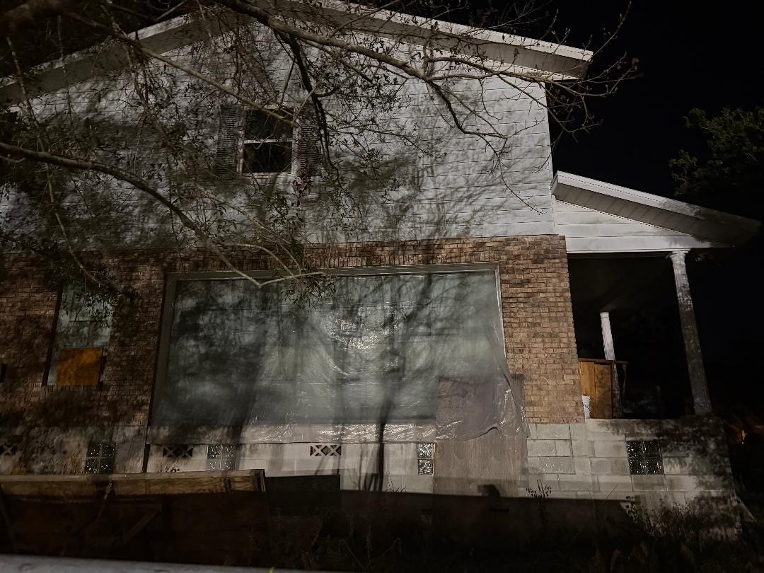 photo of a derelict house at night with shadows of trees giving it a haunted look