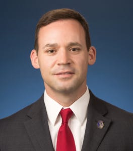White man in a black suit with a white shirt and red tie