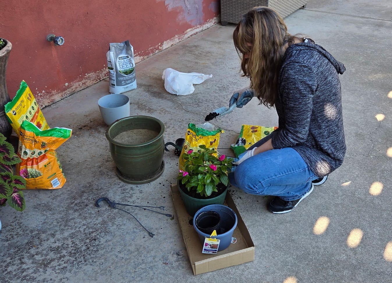 Photo of me transferring some vinca flowers to a hanging basket and surrounded by bags of potting soil and flower pots.