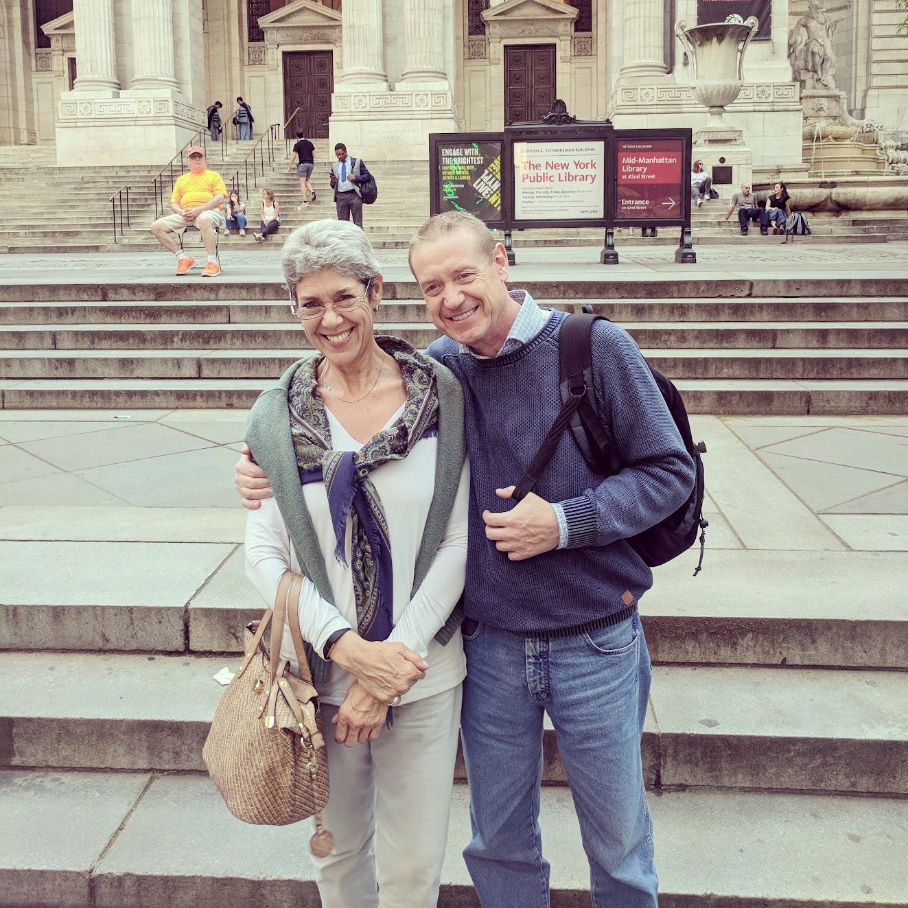 A white woman with white hair and a white man with blond hair, both in their 60s, hug in front of the New York Public Library A white woman with white hair and a white man with blond hair, both in their 60s, hug in front of the New York Public Library