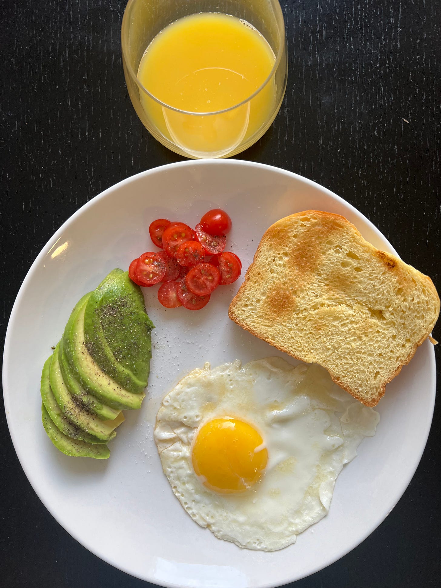 A beautifully plated breakfast featuring a sunny-side-up egg, sliced avocado, fresh tomato, and toasted bread, served with a glass of orange juice. Photographed by Liat Portal for Foodie Disorder, this image captures the vibrant simplicity of a wholesome Mediterranean-inspired meal.