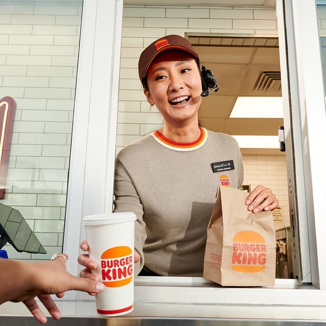 a burger king employee handing over a drink and a bag of food to a customer at a drivethru a burger king employee handing over a drink and a bag of food to a customer at a drivethru