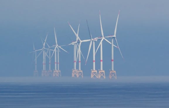 Offshore wind turbines stand in the misty ocean.