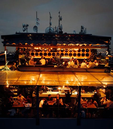 Dj tocando, comida servida en la mesa y vista de una de las terrazas bar en CDMX desde las alturas.