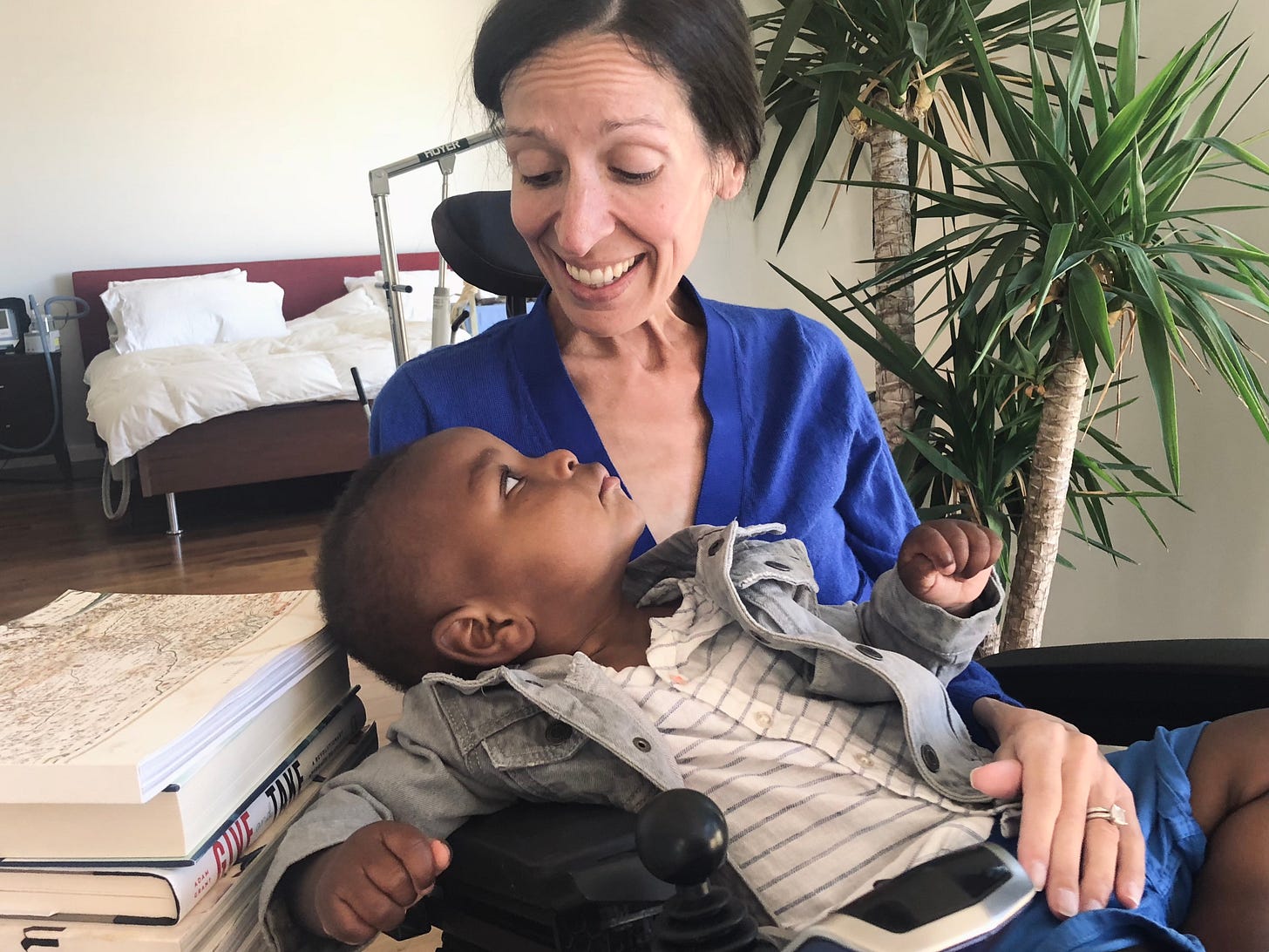 A white woman in a wheelchair (Sarah) holds a Black baby in a jean jacket (Khalil)