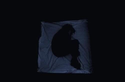 This may contain: the silhouette of a person sitting on a sheet in the dark