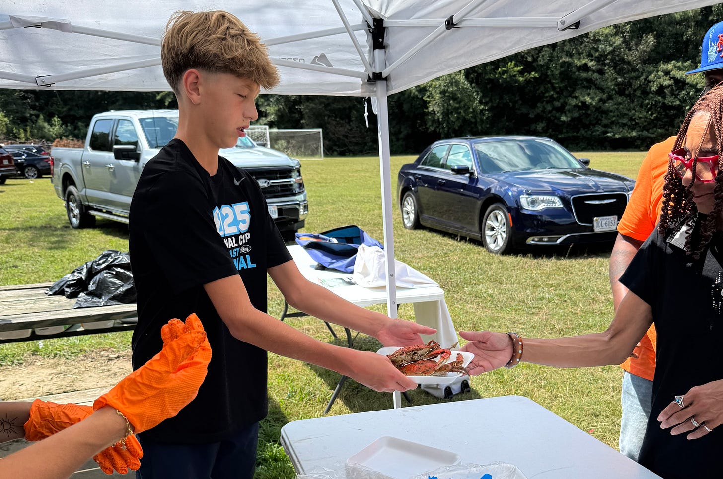 Our youngest, Ciaran, under a white tent, serving a plate of crab to a cookout guest.