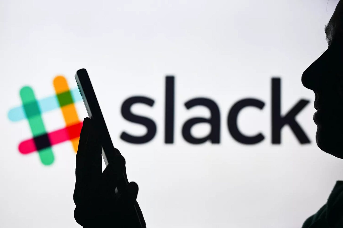 n image of a woman holding a cell phone in front of the Slack logo displayed on a computer screen, on April 29, 2024, in Edmonton, Canada.