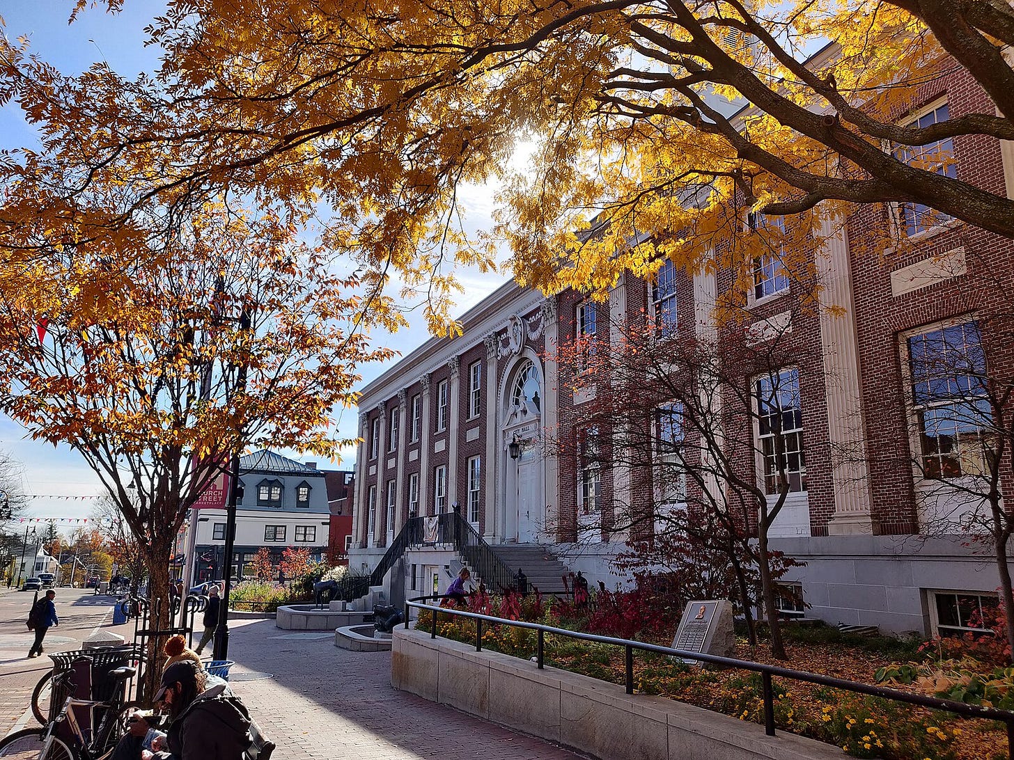 Burlington City Hall in Vermont, framed by golden autumn trees. People sit on benches and walk along the brick-paved Church Street as sunlight filters through the leaves. Burlington City Hall in Vermont, framed by golden autumn trees. People sit on benches and walk along the brick-paved Church Street as sunlight filters through the leaves.