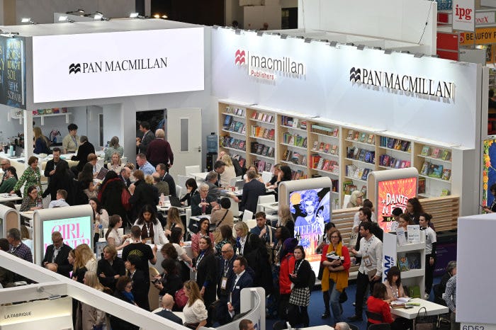 The Pan Macmillan booth at the London Book Fair, with bookshelves and many attendees. The Pan Macmillan booth at the London Book Fair, with bookshelves and many attendees.