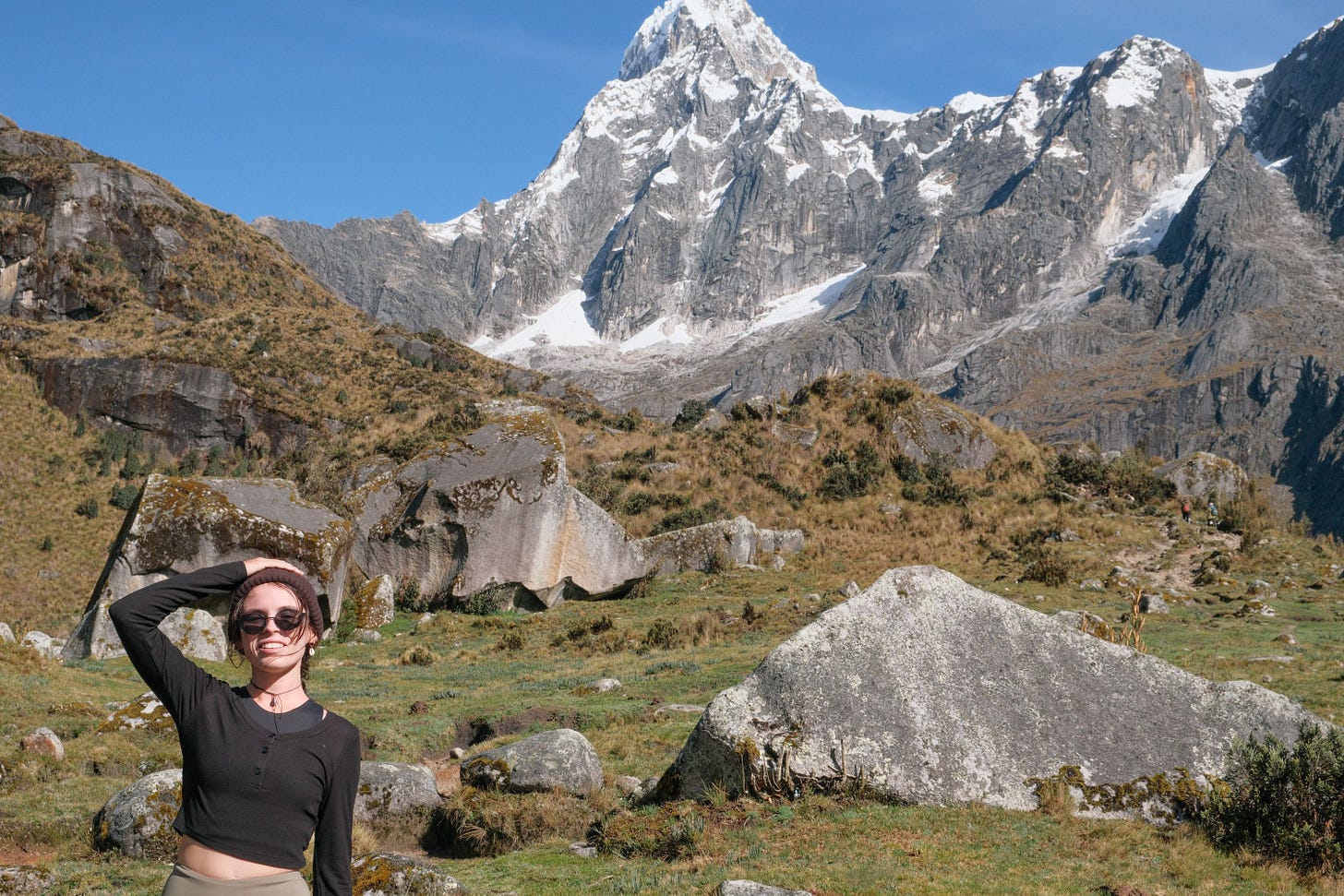 Woman smiling in front of large boulders and snow-capped peaks on the Santa Cruz Trek, Peru.