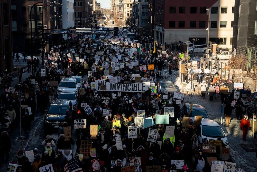 A huge anti-ICE protest in Minneapolis on January 30, 2026. Protesters are holding signs, and one banner reads "MN INVINCIBLE"