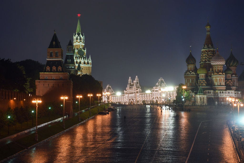 Night view of Moscow's Red Square with the Kremlin and Saint Basil's Cathedral illuminated, reflected on wet streets after rain.