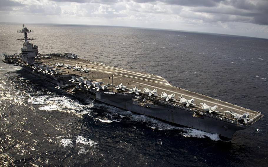 Aerial view of the aircraft carrier USS Gerald R. Ford underway at sea with fighter jets parked on the flight deck.