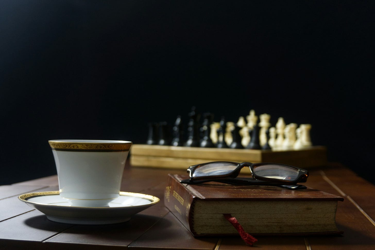 Book, glasses, and coffee with a chessboard in the background. Book, glasses, and coffee with a chessboard in the background.