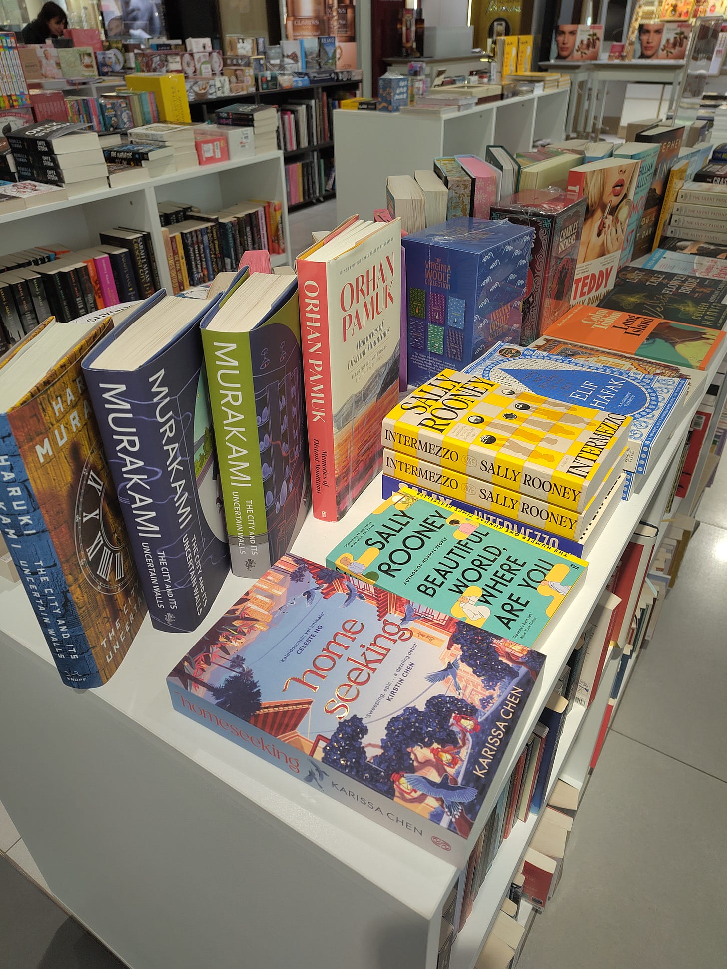 A prominent table display in a bookstore, featuring books by Haruki Murakami, Intermezzo by Sally Rooney, and Homeseeking by Karissa Chen.