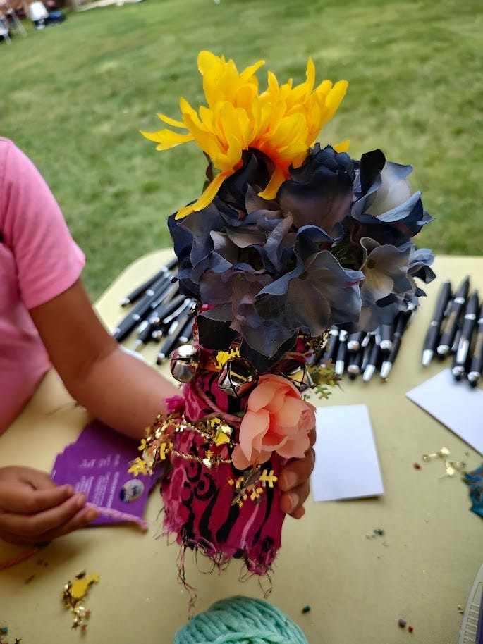 Plastic bottle maraca with yellow and dark blue flowers and bells with a textile covering.