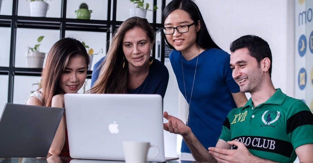 four people watching on white MacBook on top of glass-top table