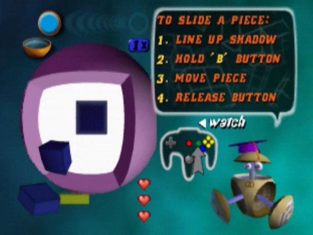 A screenshot of the Tetrisphere tutorial, as it lays out what you need to do. A robot says, "1. Line up shadow, 2. Hold 'B' button, 3. Move piece, 4. Release button." There's a small sphere to the left, and an option to watch this all in motion, as well. 
