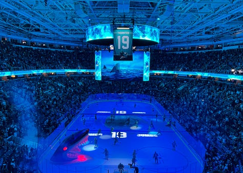 Photo 1: Image of woman in Sharks jersey smiling outside arena; Photo 2: Image of Joe Thornton ice sculpture; Photo 3: Image of Joe Thornton coming through Shark head on ice; Photo 4: image of two women smiling with ice rink behind them; Photo 5: Image of Shark head and chairs on ice for ceremony; Photo 6: Image of Joe Thornton on big screen; Photo 7: Image of Thank You Joe box where jersey was raised with family behind it; Photo 8: Image of ice rink with Shark head and players; Photo 9: Image of #12 and #19 jersey's hanging in the rafters of the arena